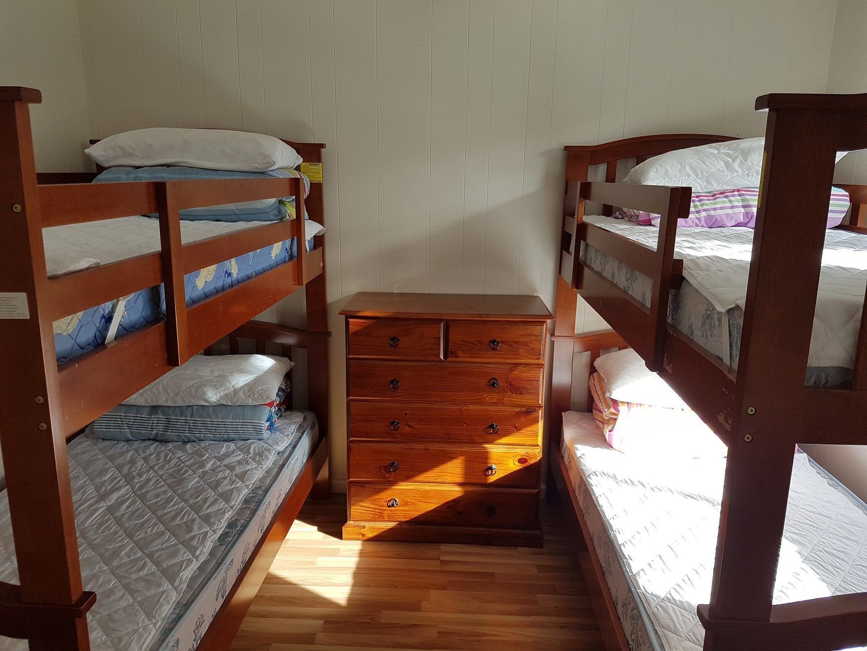A dormitory room with bunk beds, a wooden dresser, and a window providing natural light.