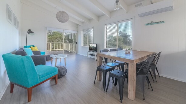 A spacious living area with a wooden dining table, teal sofa, and a TV. - 63 Marlin by Smiths Beach (Smiths Beach)