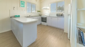 A modern kitchen with white cabinetry, a central island, a microwave, and a stove. - 63 Marlin by Smiths Beach (Smiths Beach)