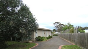 A residential street with a paved driveway, a wooden fence, and a house with a flat roof. - 5 Little Penguin Cottage in Cowes (Cowes)