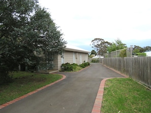 A single-story house with a flat roof and paved driveway, set amidst a grassy area with a small bush.