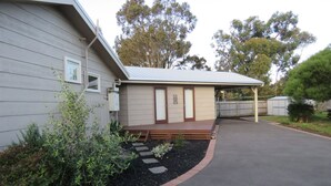 A single-story building with a covered porch, a small garden area with stepping stones, and a paved driveway. - 5 Little Penguin Cottage in Cowes (Cowes)