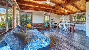 A spacious living area with a large window, a wooden ceiling, a sofa, a dining table with chairs, and a kitchen area. - 9 Boat Creek by the beach in Ventnor (Ventnor)