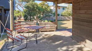 Ein überdachter Patio-Bereich mit Holztisch und -bänken, einem Betonboden und einem Holzzaun im Hintergrund.