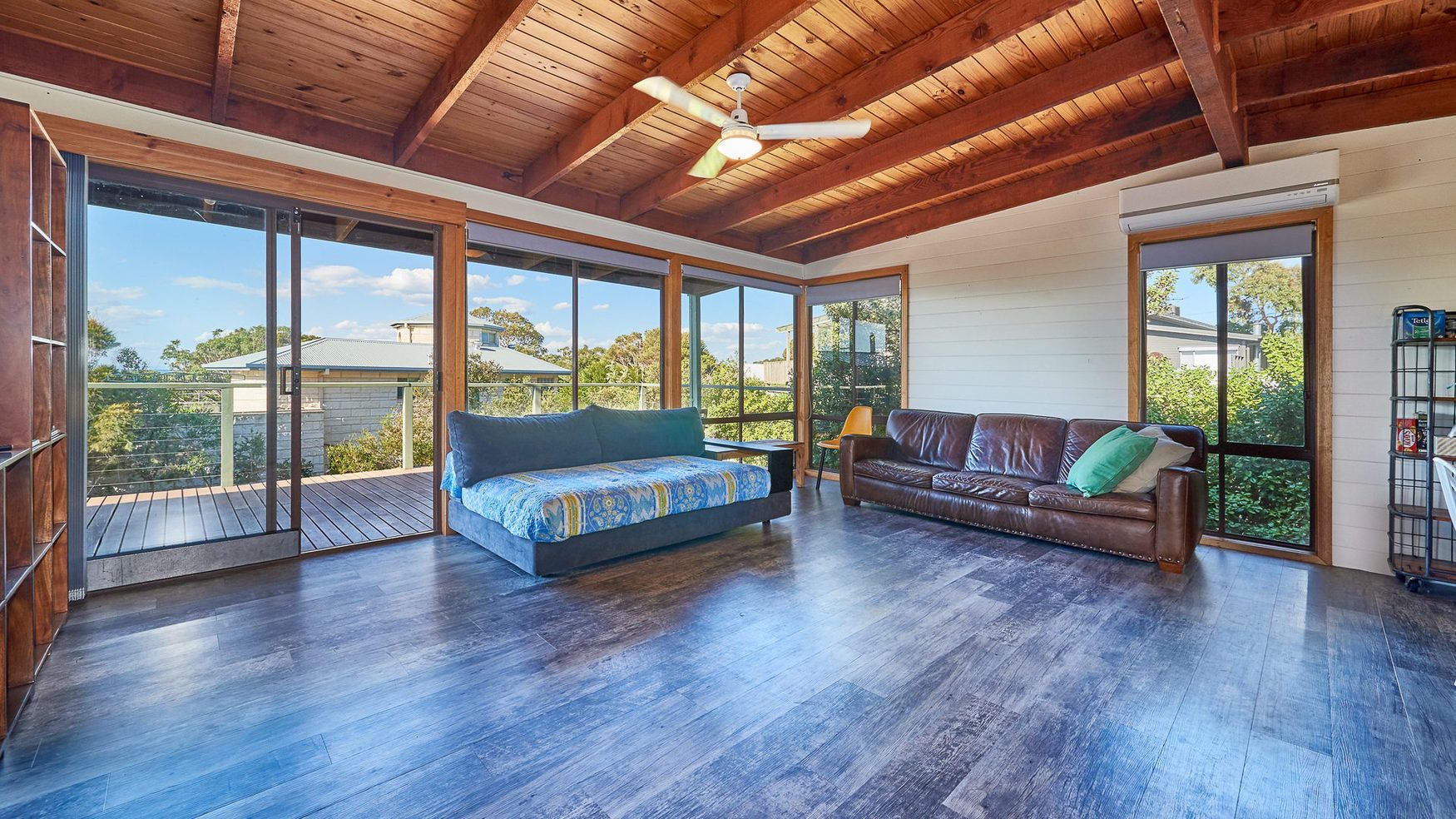 A spacious room with a large bed, a sofa, and a dining table. There are large windows providing a view of the outdoors.