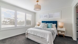 A bedroom with a bed, two bedside tables, a wall-mounted lamp, and a window with blinds. - 7 Graydens with views in Ventnor (Ventnor)