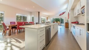 A modern kitchen with white cabinets, a central island, and a dining area with red chairs. - House on 37 Barramundi near Smiths (Smiths Beach)