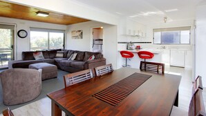 A modern living room with a wooden dining table, a brown sectional sofa, and red bar stools. - 47 Anderson with Pool in Cowes (Cowes)