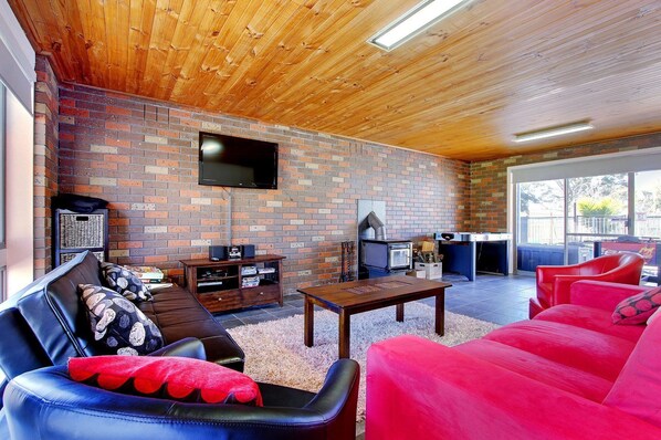 A cozy living room with a brick wall, a flat-screen TV, a fireplace, and comfortable seating. - 47 Anderson with Pool in Cowes (Cowes)