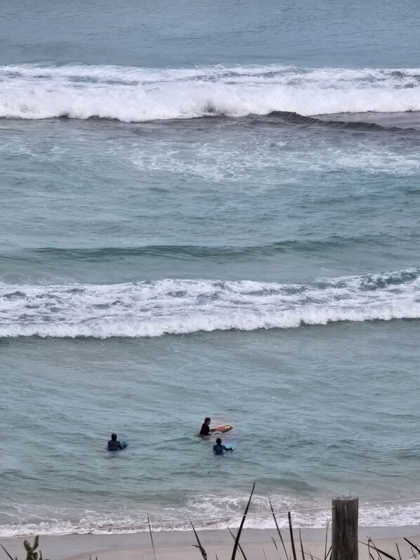 Een strand met golven en twee mensen in het water met surfplanken.