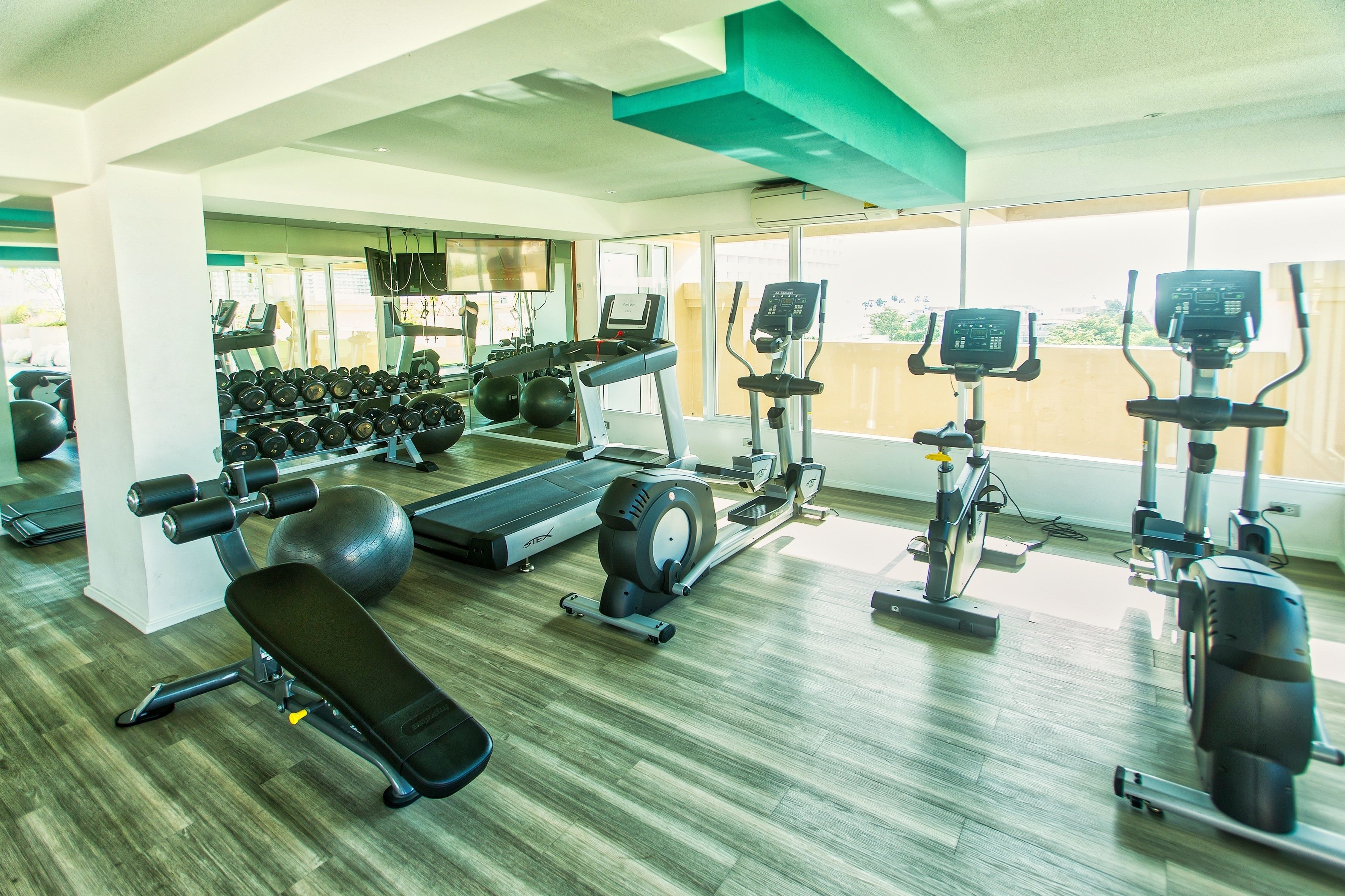 A gym with cardio machines, dumbbells, and a bench.
