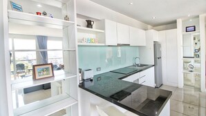 Une cuisine moderne avec des armoires blanches, un comptoir noir et un four encastré. Une fenêtre offre une vue sur l’extérieur, et une étagère expose des objets décoratifs.