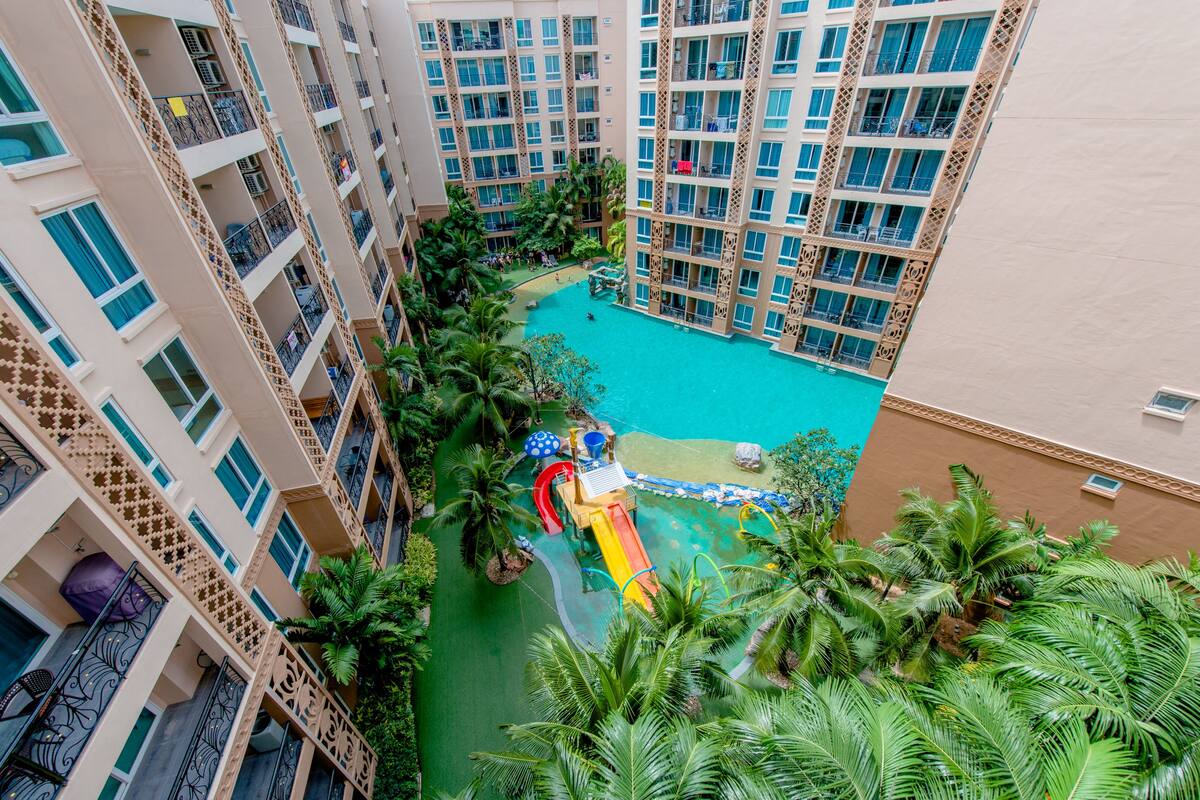 Un hotel de gran altura con un patio central que cuenta con una piscina, palmeras y un área de juegos para niños.