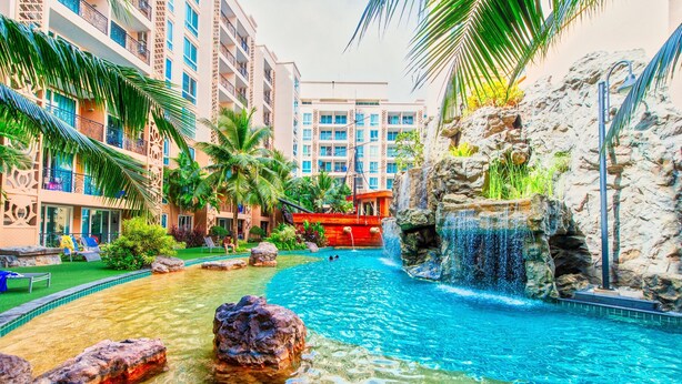 Un espace piscine d’hôtel avec une eau claire, des rochers, des palmiers et une cascade.
