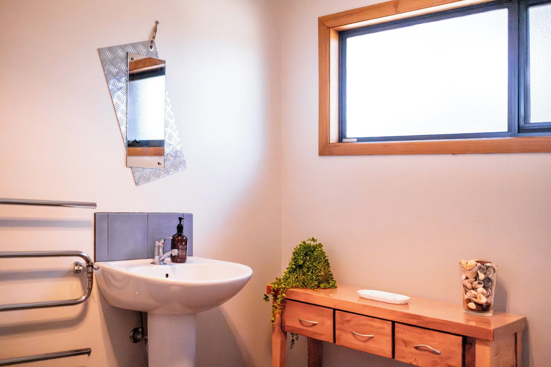 A bathroom with a white sink, a wooden vanity, a mirror, and a window.