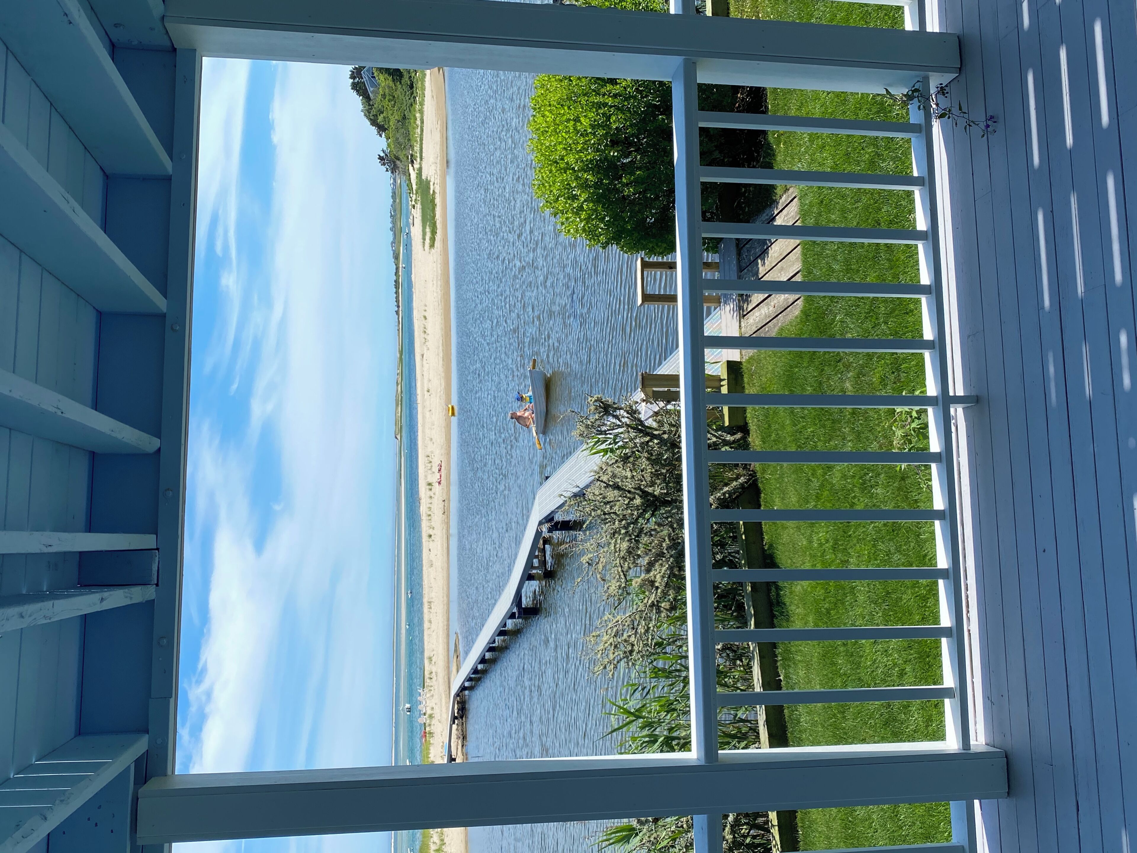 A covered deck with a view of a beach and a pier extending into the water.