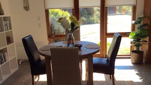 A dining area with a round table, four chairs, a vase with flowers, and a bookshelf. - Studio Rouge in heart of old Bowral only minutes walk to shops and restaurants (Bowral)