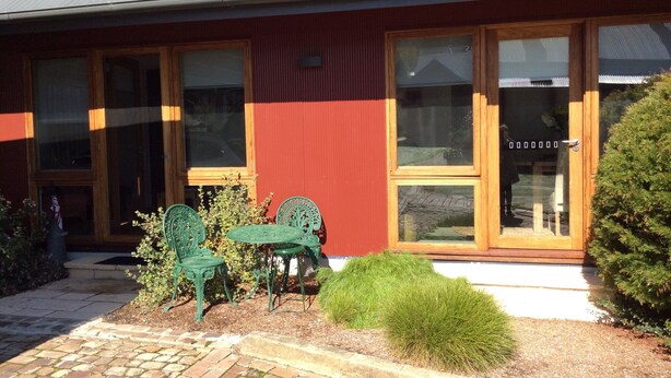 A building with a red exterior, large windows, and a small patio area with green chairs and plants. - Studio Rouge in heart of old Bowral only minutes walk to shops and restaurants (Bowral)