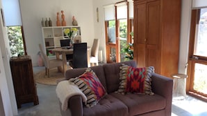 A living room with a brown sofa, a coffee table, and a bookshelf. - Studio Rouge in heart of old Bowral only minutes walk to shops and restaurants (Bowral)