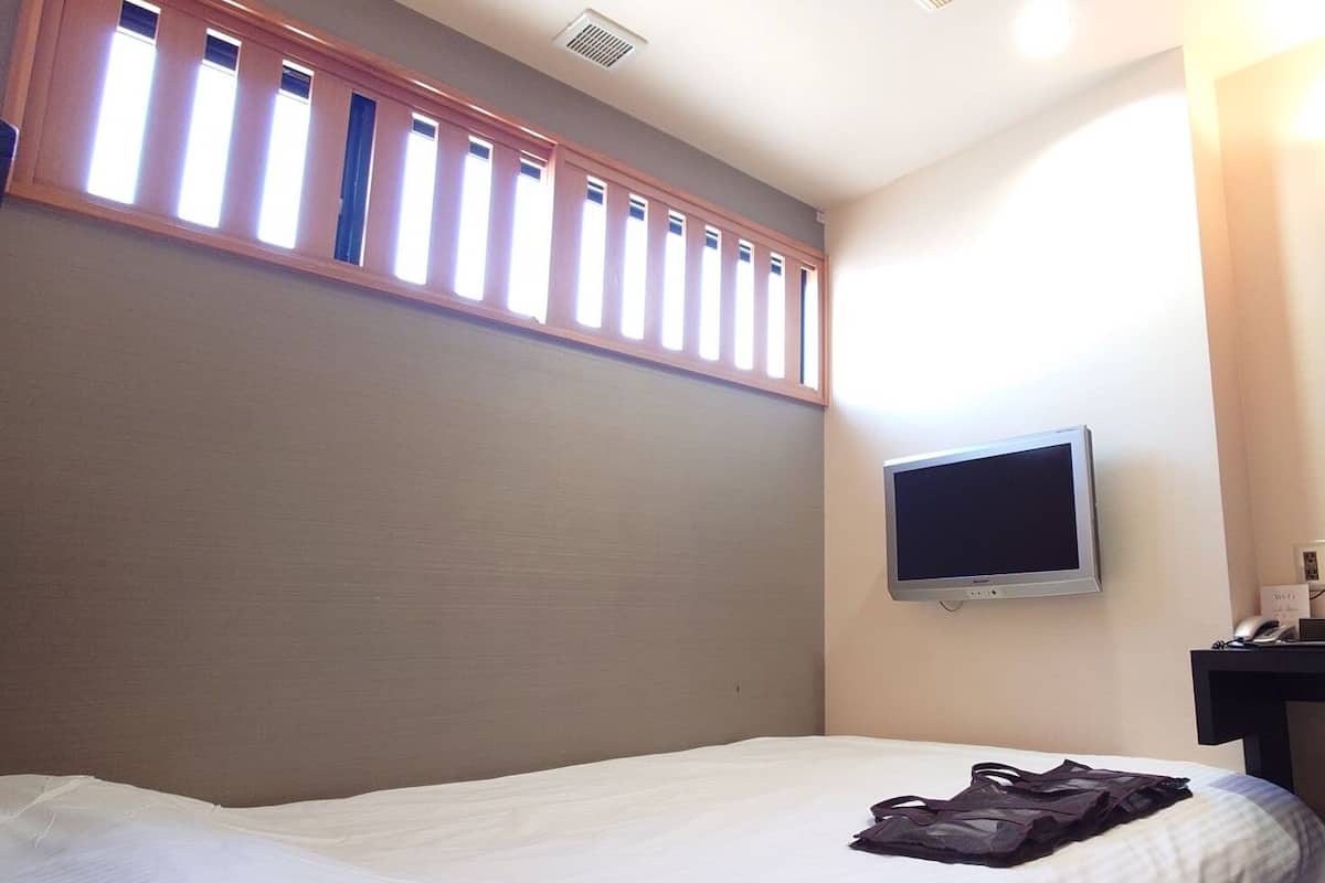 A hotel room with a bed, a TV mounted on the wall, and a window with blinds.