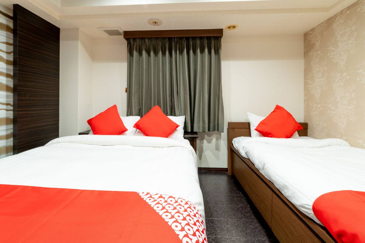 Une chambre d’hôtel avec deux lits, chacun doté d’une literie rouge et blanche, une fenêtre avec des rideaux gris et une tête de lit en bois.