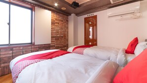 Habitación de hotel con dos camas, un muro de ladrillo, una puerta de madera y un equipo de aire acondicionado.