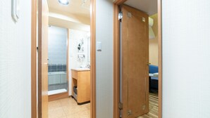 Habitación de hotel con puerta de madera, baño con lavamanos y espejo, y un sofá azul en la esquina.