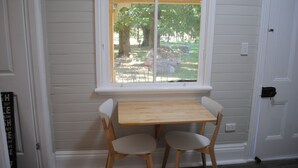 Een gezellig eetgedeelte met een houten tafel en twee stoelen, een raam met uitzicht op een tuin, en witte wandpanelen.