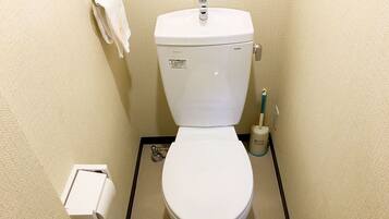 A standard white toilet with a TOTO brand label, a toilet paper holder, and a bidet spray on the right side.