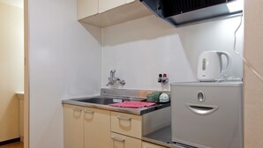 A compact kitchenette with a sink, a kettle, and a small refrigerator. - Guesthouse SAYURI 2 (Osaka)