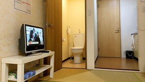 A hotel room with a television on a white stand, a toilet, and a wooden door. - Guesthouse SAYURI 2 (Osaka)