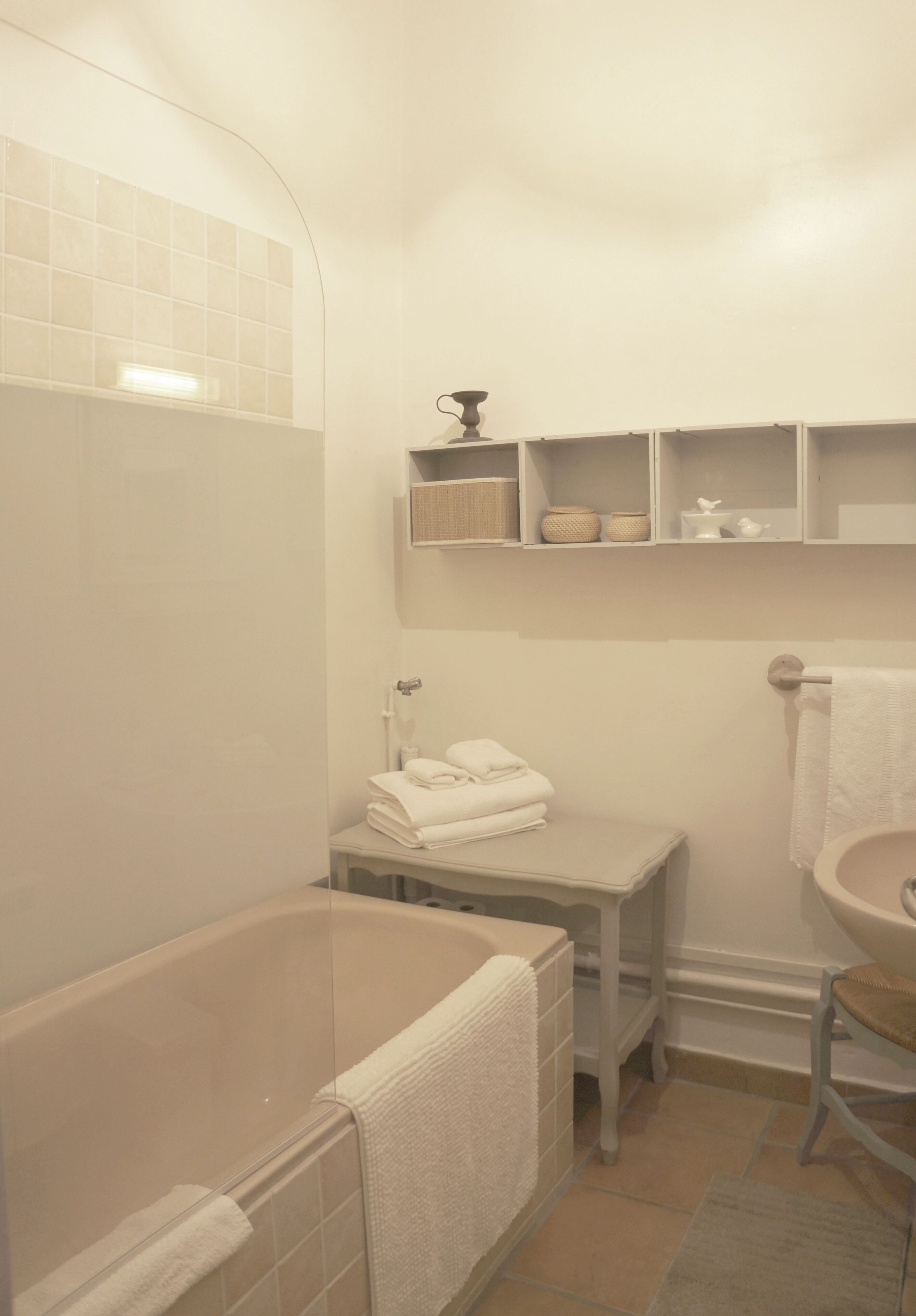 Un bagno con una vasca, un lavabo e un water. Sopra il lavabo ci sono mensole con articoli da toilette.