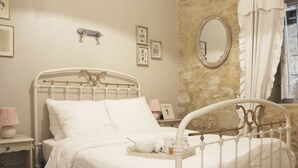Ein weißes Metallbett mit Kopfteil, ein Nachttisch mit Lampe und gerahmte Bilder an der Wand.