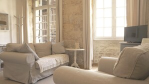 Ein Wohnzimmer mit einem beigen Sofa, einem kleinen runden Tisch und einem Fernseher auf einem Schrank.