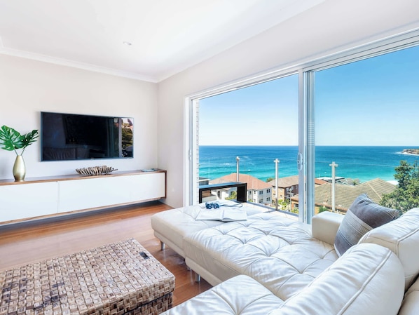 A modern living room with a large window, a flat-screen TV, a white sofa, and a wooden coffee table.