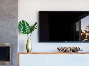 A modern living room with a flat-screen TV mounted on the wall, a gold vase with a plant, and a wooden shelf with a decorative piece.
