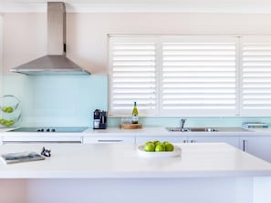 A modern kitchen with a central island, a built-in stove, a stainless steel range hood, and a window with white blinds.
