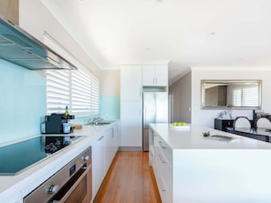A modern kitchen with a central island, built-in oven, and a large window with blinds.
