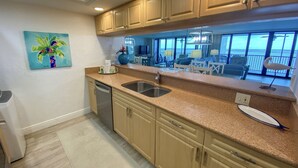 A kitchen with wooden cabinets, a dishwasher, and a large window overlooking a balcony. - Sanibel Harbour Resort Harbour Tower 714:     Coastal condo with a festive lanai (Fort Myers)