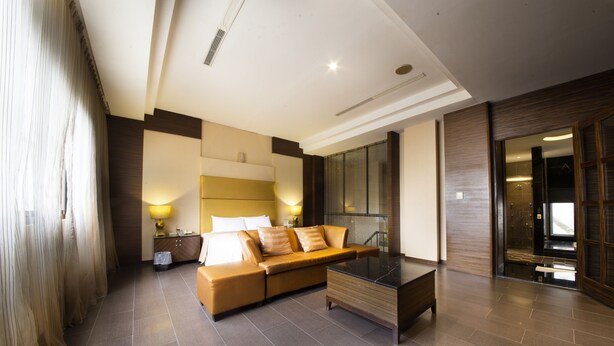 A modern hotel room with a sofa, a glass coffee table, and a large mirror.