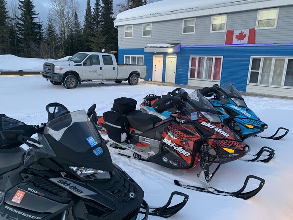 A snowmobile parked in front of a building with a Canadian flag, a truck, and snow on the ground. - Executive Suites (Chapleau)