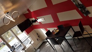 Un comedor moderno con un diseño geométrico rojo y blanco en la pared, una mesa redonda con sillas y una lámpara colgante.