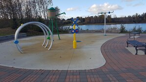 Un parque infantil con fuente de agua, estructura de madera y banco junto a un lago.