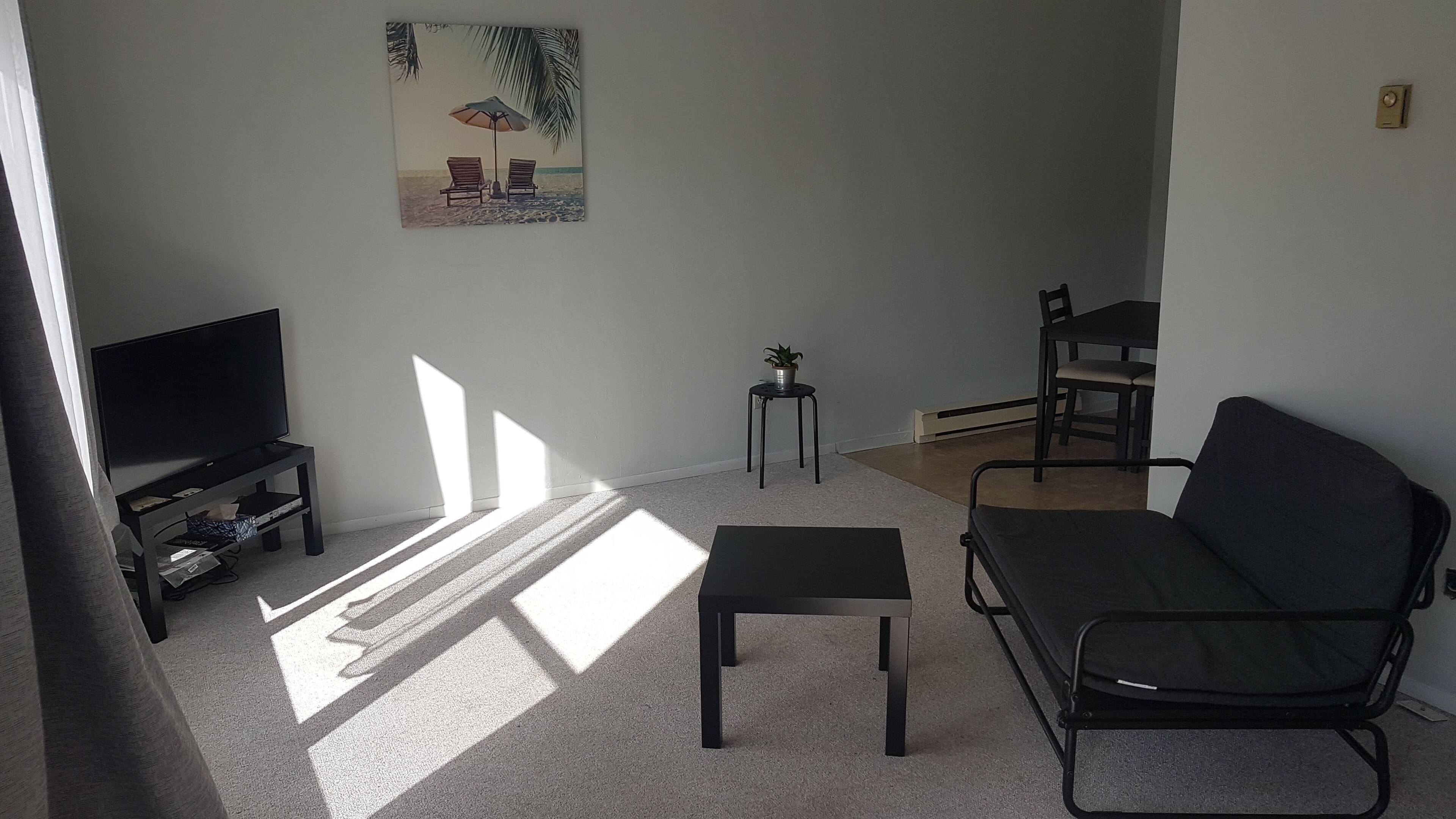 Una sala de estar con televisión, un sofá, una mesita y un cuadro de una playa.