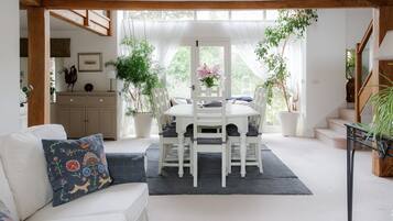 A dining area with a white table and chairs, surrounded by potted plants and a staircase.