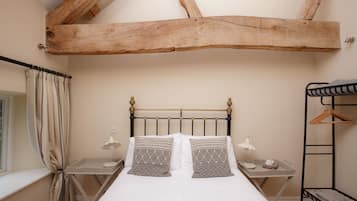 A bedroom with a wooden ceiling beam, a bed with patterned pillows, bedside tables with lamps, and a hanging rack.