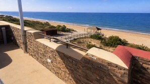 A coastal view with a stone wall, a metal pole, and a beach area with a wooden structure. - Spectacular Penthouse, authentic 1st line beach, 70 m2 terrace  (Rota)
