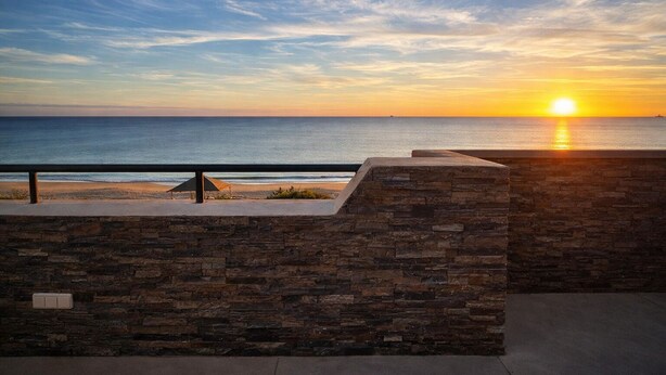 A sunset view from a balcony with a stone wall and a metal railing overlooking the beach. - Spectacular Penthouse, authentic 1st line beach, 70 m2 terrace  (Rota)