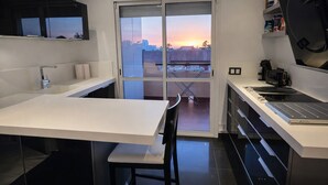 A modern kitchen with a large island, a built-in oven, and a view of the sunset through the sliding glass door. - Spectacular Penthouse, authentic 1st line beach, 70 m2 terrace  (Rota)