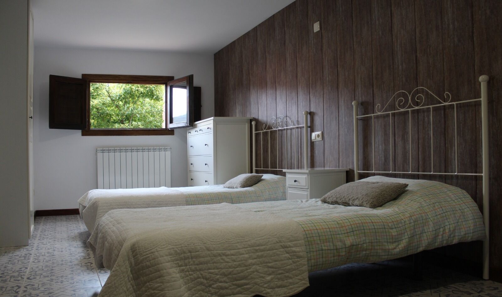 Een slaapkamer met twee bedden, een kledingkast, een radiator en een raam met uitzicht op groen.